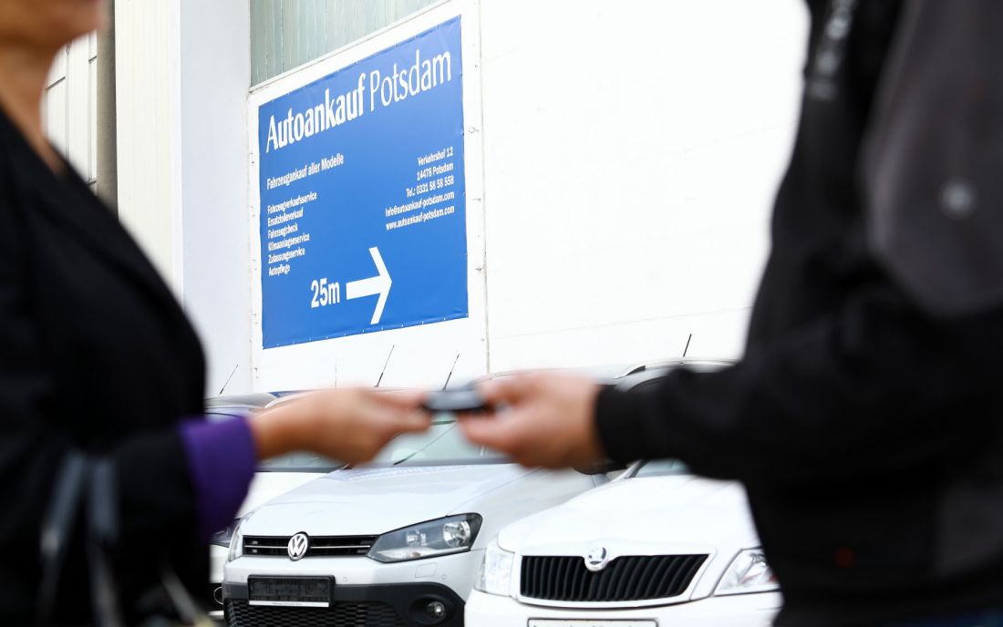 Kundin bekommt einen Autoschlüssel überreicht, im Hintergrund ist ein Banner von Autoankauf Potsdam mit Kontaktdaten und Leistungen zu sehen